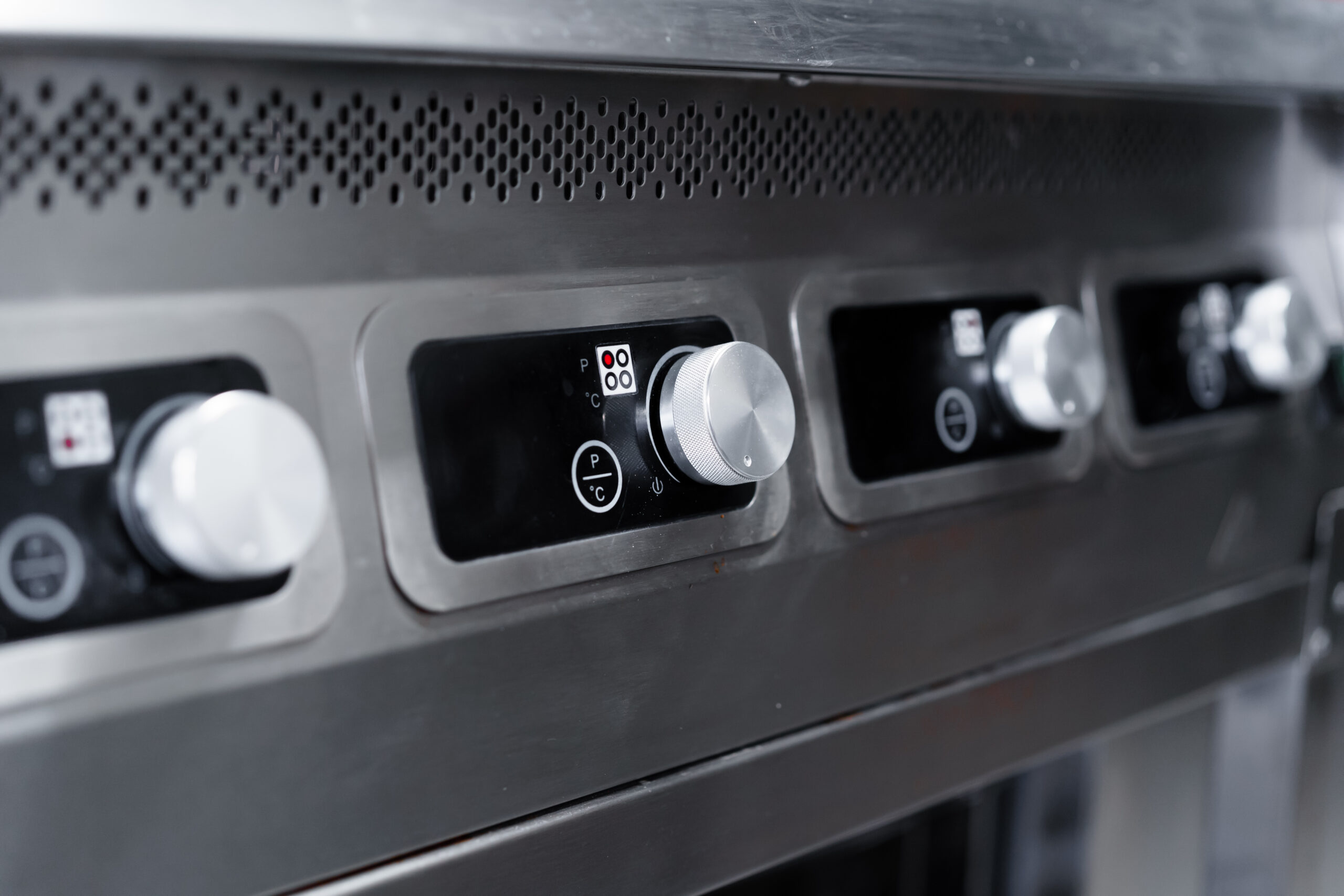 A closeup of the temperature control knobs of a commercial cooking appliance.